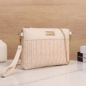 Detail of beige woven crossbody bag with gold chain strap and metal nameplate decoration