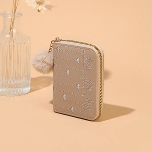 Dettaglio portafoglio beige con zip, ricamo a cuore e ciondolo morbido a forma di pompon