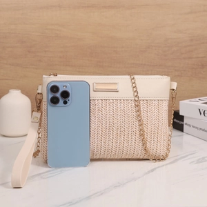 Detail of cream woven envelope bag with gold chain and leather strap beside a phone