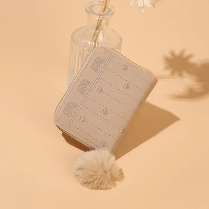 Dettaglio del portafoglio in pelle PU beige con ricamo a farfalla e ciondolo a pompon