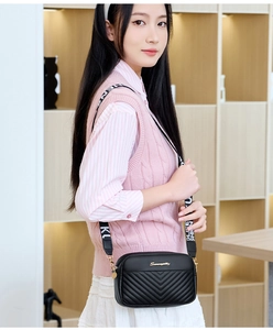 Detail of black V-quilted crossbody bag with golden logo and patterned fabric strap