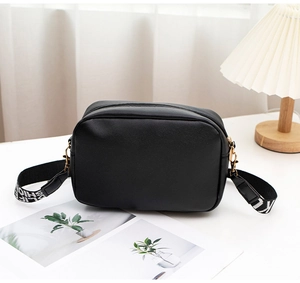 Detail of black leather square crossbody bag with embroidered lines and wide shoulder strap