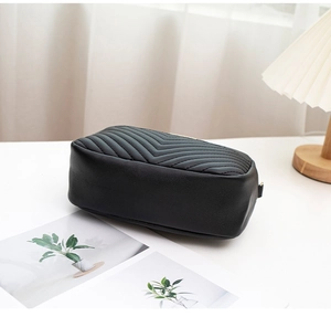 Detail of black V-quilted faux leather crossbody bag on a minimalist white desk setting