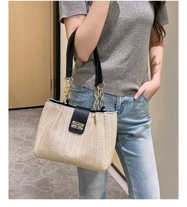 Detail of beige straw bag with black leather flap and gold metal chain strap on model