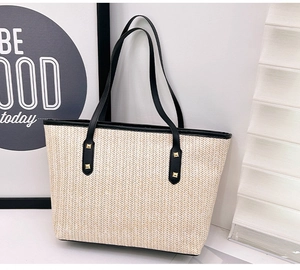 Detail of woven straw tote bag featuring herringbone pattern and black leather straps