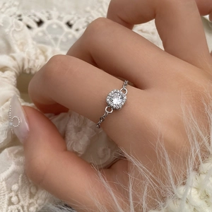 Close-up of a halo cubic zirconia ring with a stylish silver chain band on a soft background