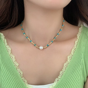 Collier en perles dorées avec perles turquoise et perle blanche sur un mannequin