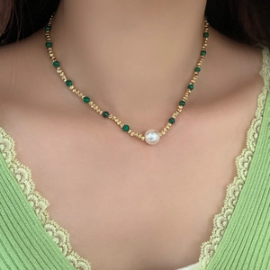 Détail d'un collier de perles et malachite avec perles dorées sur vêtement en dentelle