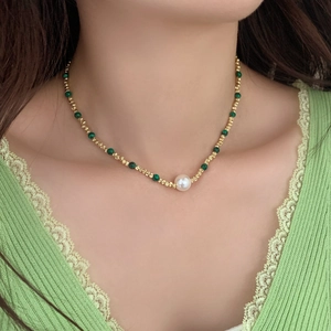 Détail d'un collier de perles dorées avec pierres turquoise et grosse perle blanche