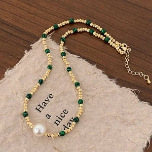 Détail d'un collier de perles dorées avec perles de malachite verte et une grosse perle blanche