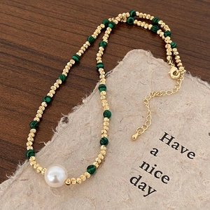 Détail du collier à perles avec perles dorées facettées, malachite verte et grande perle blanche
