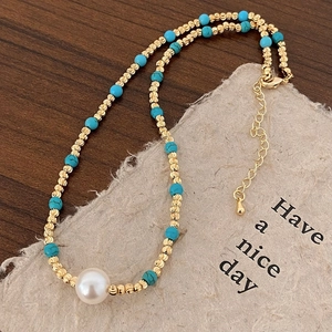 Détail du collier de perles avec billes dorées, pierres turquoise et une grande perle blanche