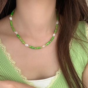 Green bead and freshwater pearl necklace with gold accents worn by a model on lace clothing
