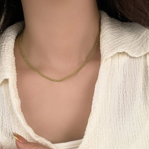 Detailed close-up of a double-layered green beaded necklace on a white textured shirt