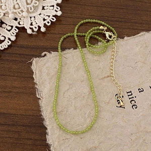 Close-up of green beaded choker with gold clasp on rustic paper and lace background