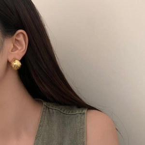 Close-up of a gold hammered ball earring on a model with minimalist French C-shape texture
