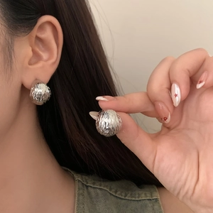 Detail of silver C-shaped stud earrings with textured surface worn by a model