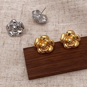 Detail of gold and silver camellia flower stud earrings on wooden and linen display