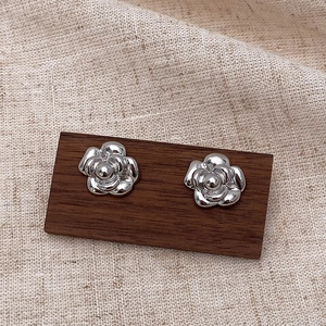 Macro shot of silver camellia petal earrings with a polished mirror finish on wood