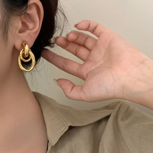 Gros plan de boucles d'oreilles géométriques dorées à triple anneau portées par un mannequin