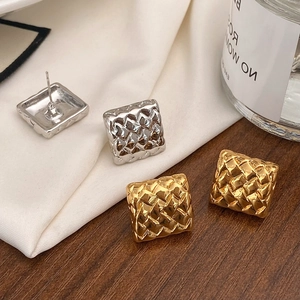 Détail de boucles d'oreilles carrées tressées dorées et argentées sur fond de soie