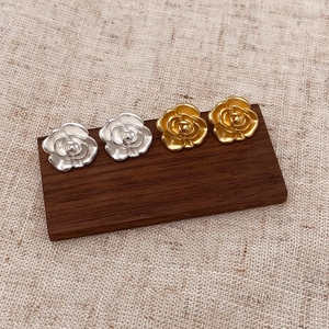 Elegant matte camellia stud earrings in gold and silver finish on a wooden stand