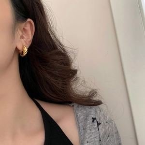 Close-up of golden croissant hoop earring with spiral texture on a model's ear
