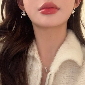 Detailed view of pearl bow earrings and fine chain necklace on a model's neck