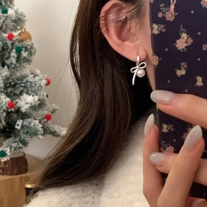 Close-up of bowknot pearl earrings worn by a model in a festive Christmas setting