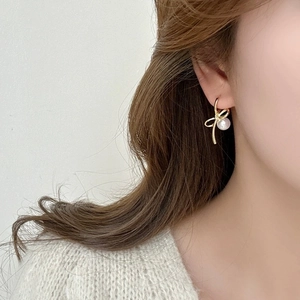 Close-up of golden bow earrings with round white pearl pendants worn by a female model