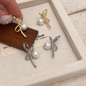 Elegant bow knot pearl drop earrings in gold and silver finish on jewelry display