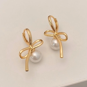 Close-up of golden bow earrings with white pearl pendants on light background