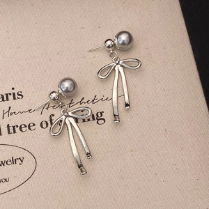 Détail de boucles d'oreilles nœuds argentés avec perles violet clair sur fond canevas
