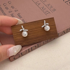 Boucles d'oreilles nœud et perle avec zircons sur présentoir en bois sombre