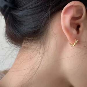 Detail of twisted gold knot hoop earrings worn by a model showing polished metallic texture