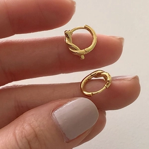Close-up of golden knotted hoop earrings held by hand showing twisted rope design details