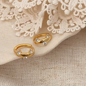 Close-up of small gold-plated hoop earrings featuring three sparkling zircon stones