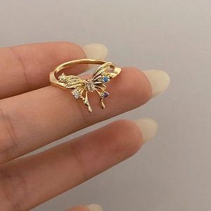 Detail of a gold butterfly ring with inlaid blue and purple zircon on a hand
