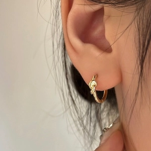 Close-up of a gold knot hoop earring worn by a model, showing sleek geometric design