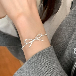 Detail of silver bow bracelet with twisted rope texture worn on a woman's wrist