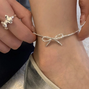 Detail of silver bow pendant anklet with shimmering crushed silver chain on ankle