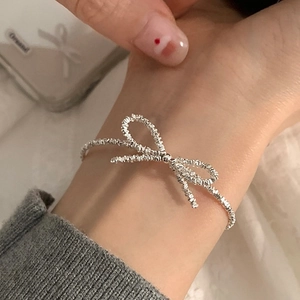 Detailed view of a shiny silver bow bracelet with crushed silver texture on a female wrist