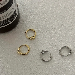 Detail of minimalist knot hoop earrings in polished gold and silver finishes on a textured base