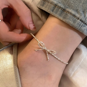 Close-up of a silver bow necklace with crushed silver texture worn on the ankle