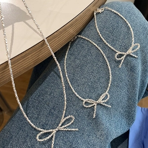 Glittering silver necklace and bracelet set with delicate bow pendants on denim