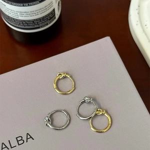 Detail view of stylish gold and silver knot hoop earrings on a minimalist display card