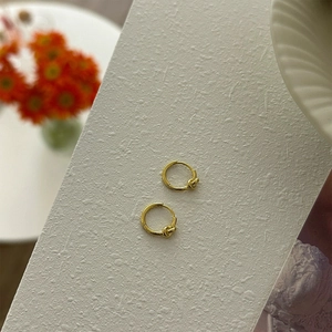 Detailed close-up of gold minimalist knotted hoop earrings on a textured white surface