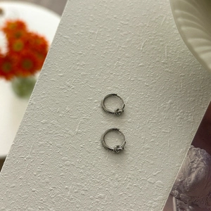 Close-up of silver knot hoop earrings on a textured white surface with floral accents