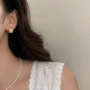 Close-up of geometric square gold earrings paired with a white pearl necklace on a model