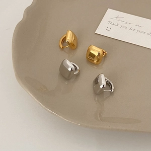 Polished gold and silver geometric square hoop earrings set on a ceramic tray